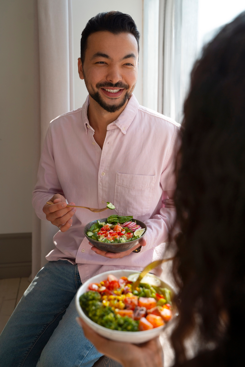 A man holds a low-carb meal bowl while talking with someone, showing how keto or low-carb eating can look in daily life.