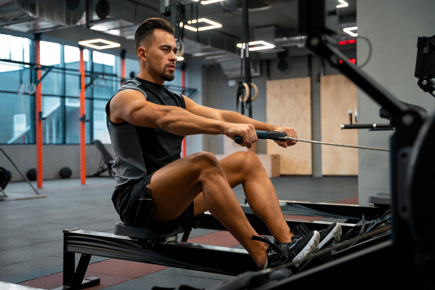 A man uses a rowing machine during an intense gym workout, illustrating how training can raise recovery demands.