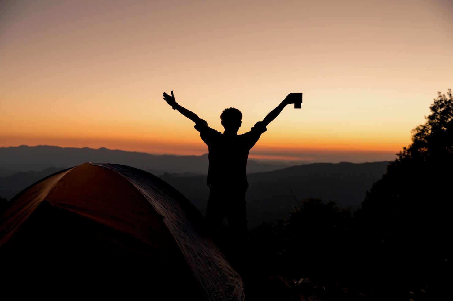 Silhouette of a person standing with arms raised in triumph at a campsite during sunrise or sunset. A tent is pitched nearby, and the background features rolling hills and a colorful sky transitioning from orange to purple. The scene conveys a sense of freedom, accomplishment, and connection with nature.