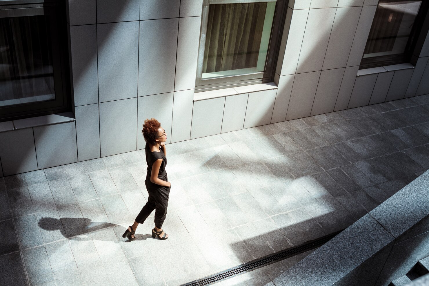 A woman takes a purposeful walk through a bright patch of afternoon sunlight between city buildings.