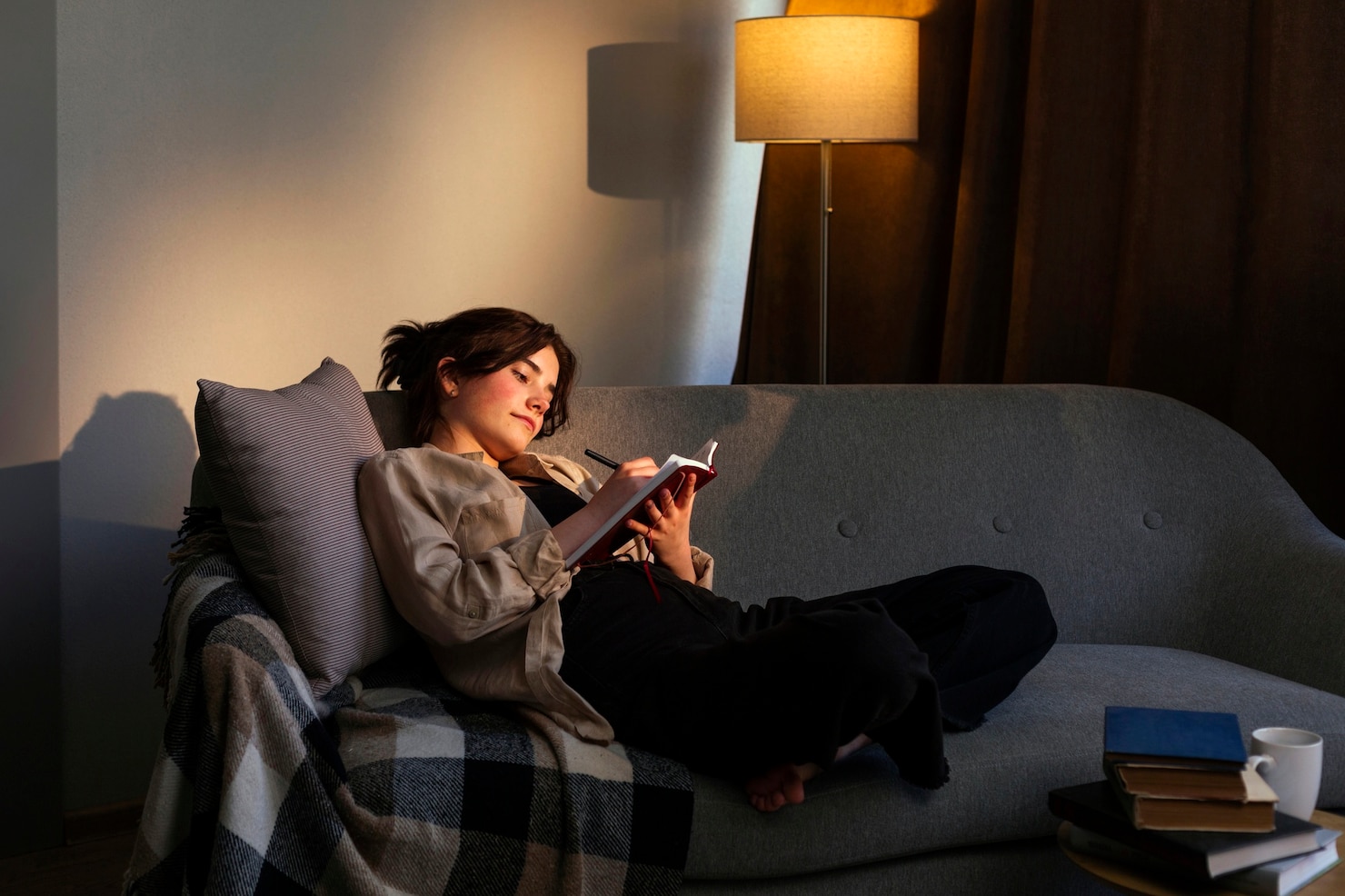 A woman writes quietly in a journal on a sofa beneath a single warm lamp.