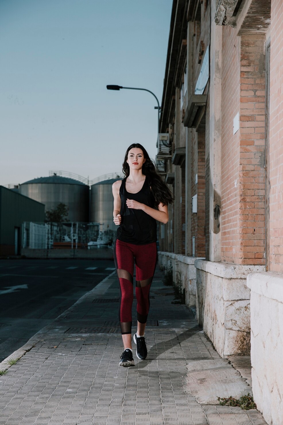 A runner jogs along a quiet industrial street in the evening.