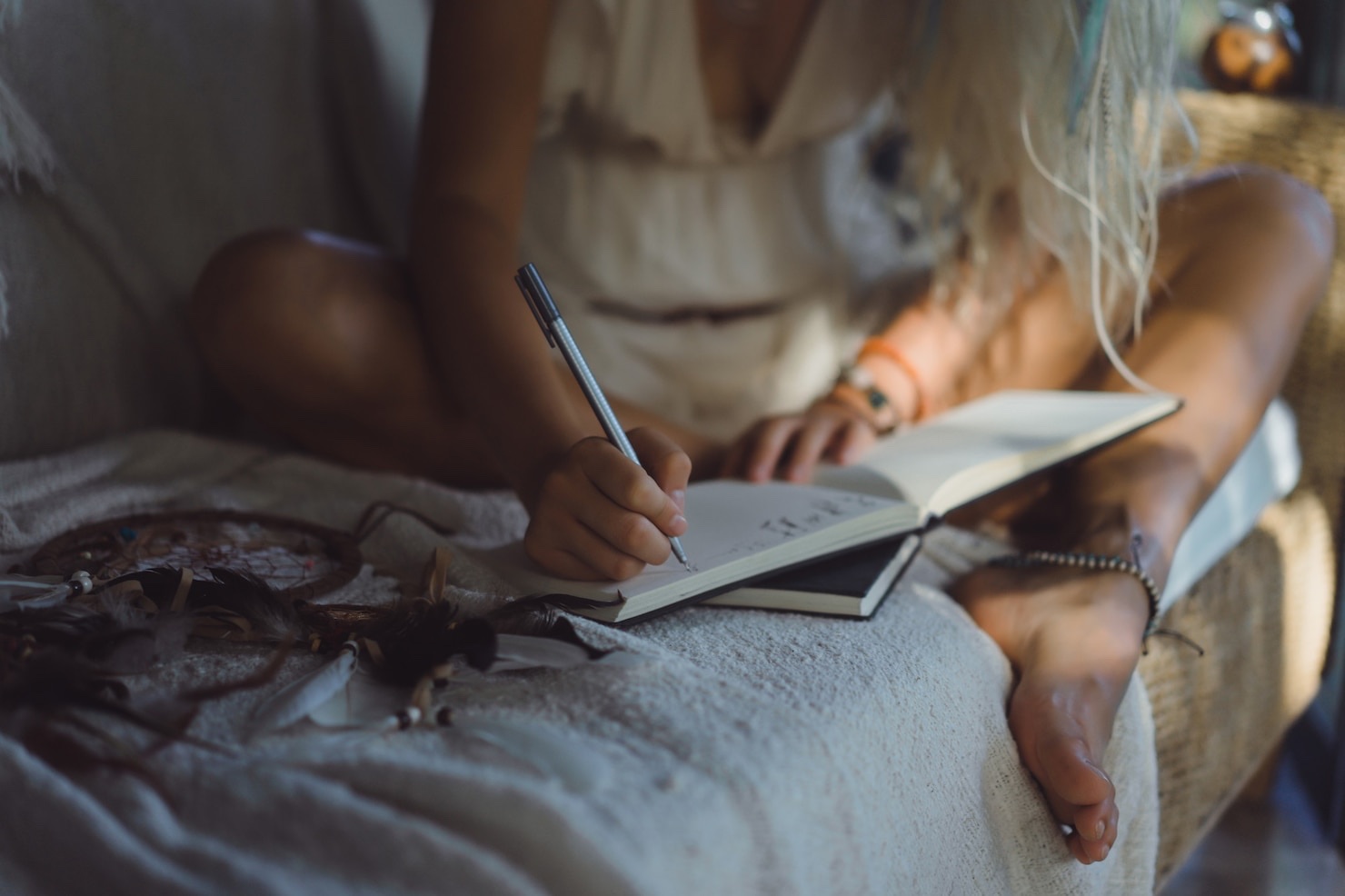 A woman writes in a notebook while seated at home.