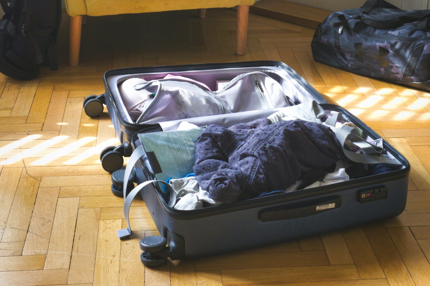 An open suitcase and travel bags sit half-unpacked on a sunlit floor, capturing the unsettled transition from traveling back to home routines.
