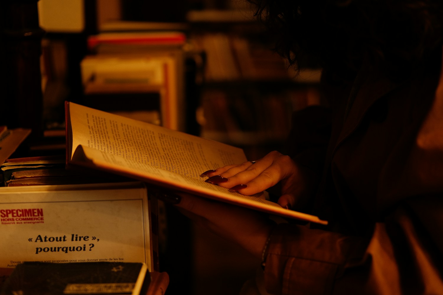 A person reads a book by low amber light in an otherwise dark room.