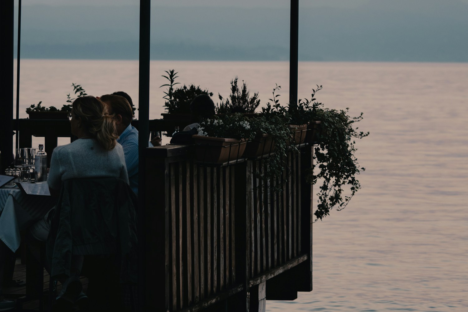 Travelers linger over dinner beside a lake at dusk, as the social and active part of a vacation day extends into the evening.